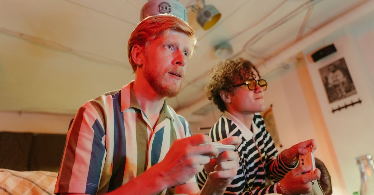 Two men playing video games with controllers and having fun in a cozy room.